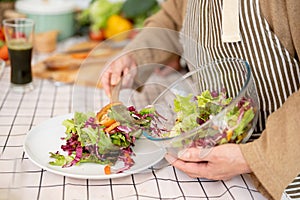 A lovely wife is serving a salad on a plate after cooking it with her husband in the kitchen
