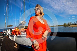 Lovely woman in a bright red suit on the background of the yacht. The blonde in sunglasses on the background of the