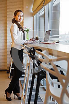 Lovely woman in business suit standing near table with laptop