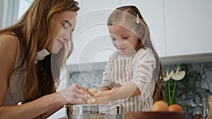 Lovely woman daughter cooking at kitchen. Mom removing pastry from child hands