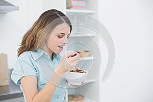 Lovely woman eating cereals while standing in her kitchen