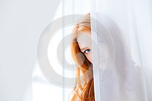 Lovely woman hiding behind white curtains