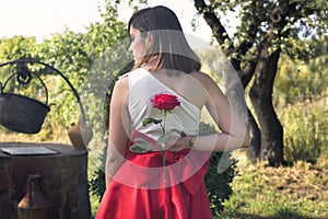 Lovely woman holding a red rose on her back