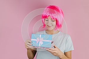 Lovely woman with pink hair holding open blue  gift box on a pastel pink background