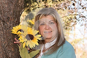 Lovely woman poses holding flowers next to tree