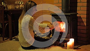 Lovely Woman Sitting On White Fluffy Carpet, Warming His Hands By The Fireplace