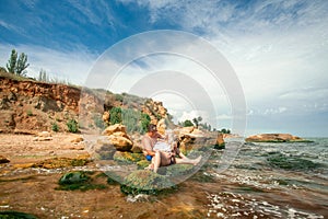 Lovely young adult couple on the rocks in the sea near the beach with big cliffs, place for text