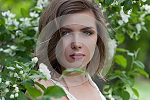 Lovely young adult woman female model with clean fresh skin, make-up and brown hair in blossom garden on green leaves background