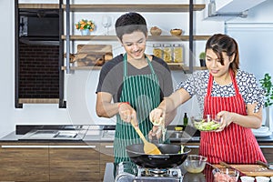 Lovely young Asian couple with casual clothes is smiling, cooking healthy food by fresh organic vegetables for breakfast, lunch