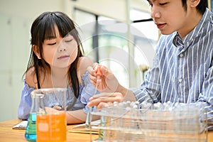 Lovely young Asian girl is concentrating, looking at her teacher while doing an experiment