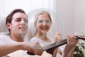 Lovely young caucasian couple or lover on bed together. Man play guitar to woman in dreamy romantic moment in bedroom. Photo of ma