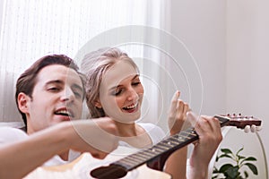 Lovely young caucasian couple or lover on bed together. Man play guitar to woman in dreamy romantic moment in bedroom. Photo of ma