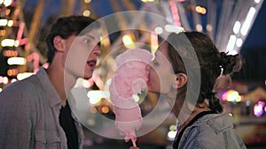 Lovely young couple at amusement park. Spending time together, eating pink cotton candy from sides. Loving couple