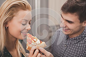 Lovely young couple eating pizza together at the kitchen
