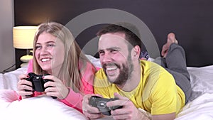 Lovely young couple having fun playing videogames in bed