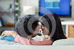 Lovely young couple kissing while watching TV on the sofa at home