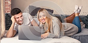 Lovely young couple with laptop lying on sofa in living room