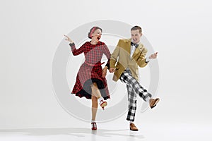 Lovely young couple, man in checkered pants and jacket, woman in red dress energetically dancing isolated over white