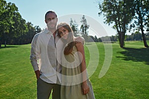 Lovely young couple smiling at camera, posing together outdoors while walking in the park on grass