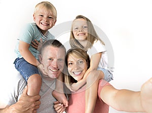 Lovely young couple taking selfie photo self portrait with stick and mobile phone carrying son and daughter on shoulders posing ha