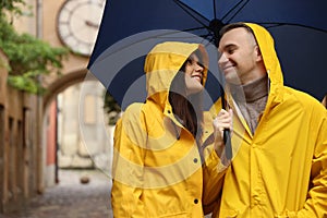 Lovely young couple with umbrella walking under rain on city street