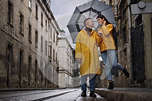 Lovely young couple with umbrella walking under rain on city street