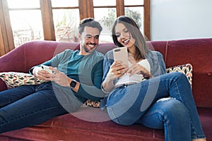 Lovely young couple using they mobile phone while sitting on sofa at home