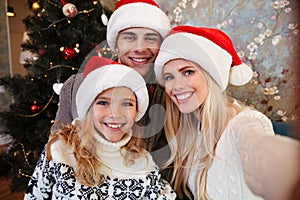 Lovely young family in Santa`s hat taking selfie near Christmas