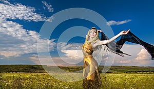 Lovely young lady posing dramatically with long black veil on green field. Blonde woman with cloudy sky in background - outdoor