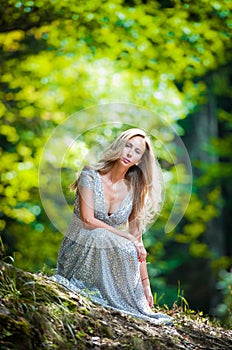 Lovely young lady wearing elegant white dress enjoying the beams of celestial light on her face in enchanted woods. Pretty blonde