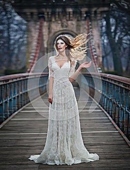 Lovely young lady wearing elegant white dress enjoying the beams of celestial light and snowflakes falling on her face.