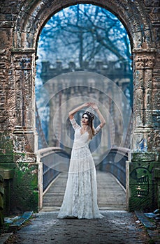 Lovely young lady wearing elegant white dress enjoying the beams of celestial light and snowflakes falling on her face.