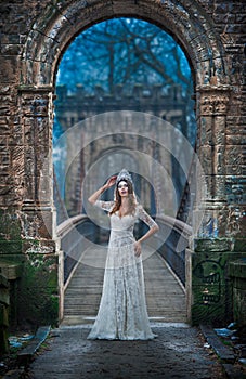 Lovely young lady wearing elegant white dress enjoying the beams of celestial light and snowflakes falling on her face.