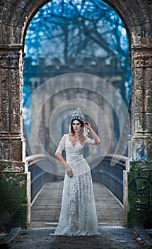 Lovely young lady wearing elegant white dress enjoying the beams of celestial light and snowflakes falling on her face.