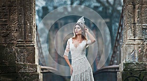 Lovely young lady wearing elegant white dress enjoying the beams of celestial light and snowflakes falling on her face.