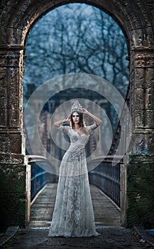 Lovely young lady wearing elegant white dress enjoying the beams of celestial light and snowflakes falling on her face.