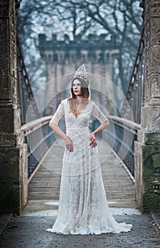 Lovely young lady wearing elegant white dress enjoying the beams of celestial light and snowflakes falling on her face.