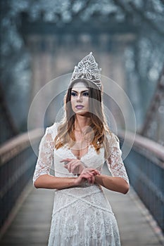 Lovely young lady wearing elegant white dress enjoying the beams of celestial light and snowflakes falling on her face.