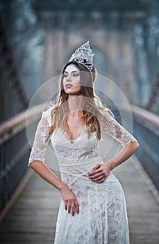 Lovely young lady wearing elegant white dress enjoying the beams of celestial light and snowflakes falling on her face.