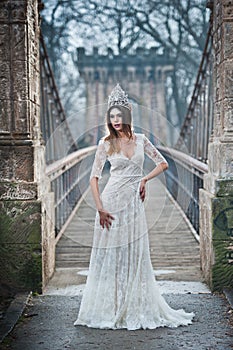 Lovely young lady wearing elegant white dress enjoying the beams of celestial light and snowflakes falling on her face.