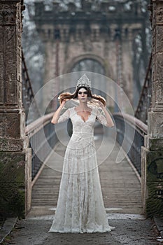Lovely young lady wearing elegant white dress enjoying the beams of celestial light and snowflakes falling on her face
