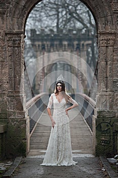 Lovely young lady wearing elegant white dress enjoying the beams of celestial light and snowflakes falling on her face