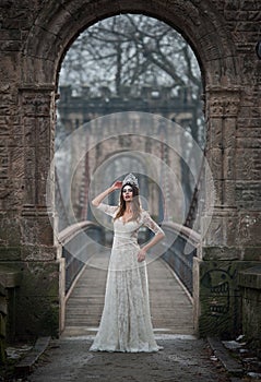 Lovely young lady wearing elegant white dress enjoying the beams of celestial light and snowflakes falling on her face