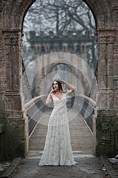 Lovely young lady wearing elegant white dress enjoying the beams of celestial light and snowflakes falling on her face