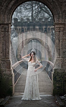 Lovely young lady wearing elegant white dress enjoying the beams of celestial light and snowflakes falling on her face