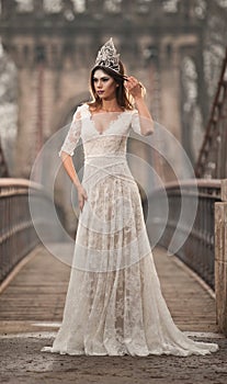 Lovely young lady wearing elegant white dress enjoying the beams of celestial light and snowflakes falling on her face.