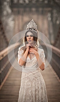 Lovely young lady wearing elegant white dress enjoying the beams of celestial light and snowflakes falling on her face.