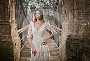 Lovely young lady wearing elegant white dress enjoying the beams of celestial light and snowflakes falling on her face.