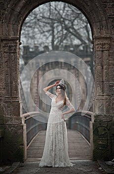 Lovely young lady wearing elegant white dress enjoying the beams of celestial light and snowflakes falling on her face.