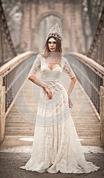 Lovely young lady wearing elegant white dress enjoying the beams of celestial light and snowflakes falling on her face.